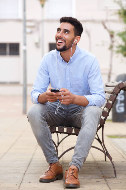 Portrait of young arabic man sitting on bench with mobile phone and earphones