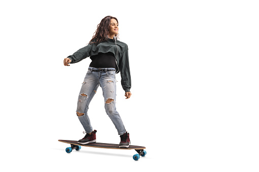 Full length profile shot of a teenage girl riding a longboard isolated on white background