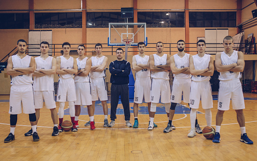 Group of people, male friends sitting on the bench together outdoors by the basketball court.