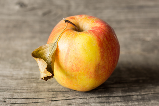 Yellow apple with red sidewalls and a dried leaf on a wooden background