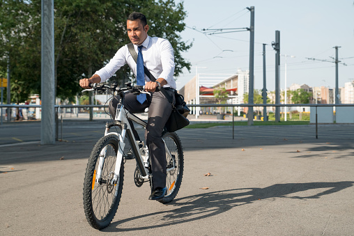 Serious businessman riding bicycle while hurrying to work. Confident young office employee leading healthy lifestyle and travelling on bike. Cycling as daily routine concept