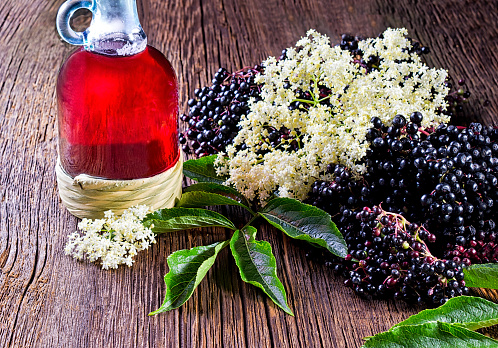 Bottle with elderberry juice and fresh berry fruits on wooden table.
