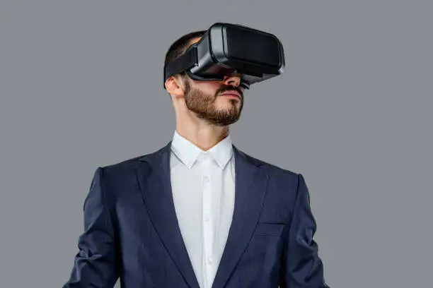 Male in a suit with virtual reality glasses on his head. Isolated on grey background.
