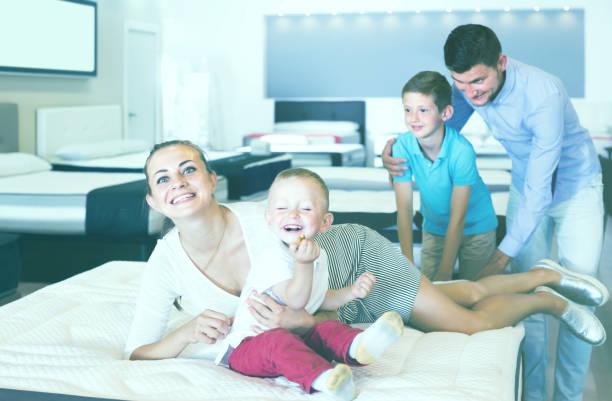 istock attractive young woman with husband and sons testing mattress in store 913729548