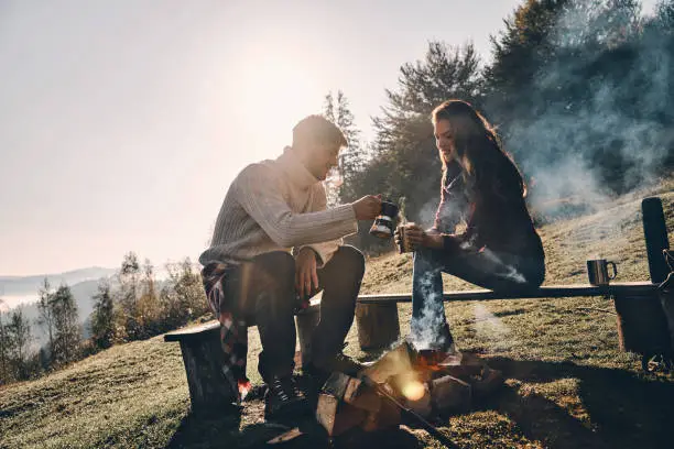 Happy young couple having morning coffee while camping in mountains