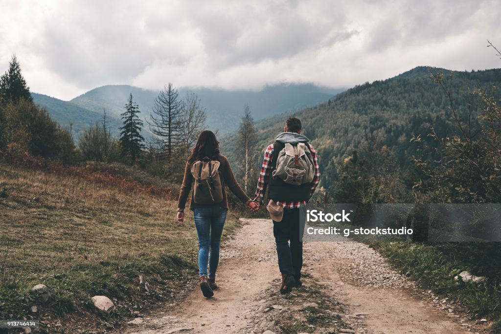 Always side by side. Full length rear view of young couple holding hands while hiking in mountains Hiking Stock Photo