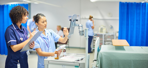 a young nurse checks the dosage on her digital tablet supervised by her staff nurse