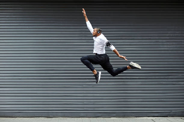 Full length of sporty young man jumping against shutter. Side view of fit male jogger is exercising in mid-air. He is wearing sports clothing.