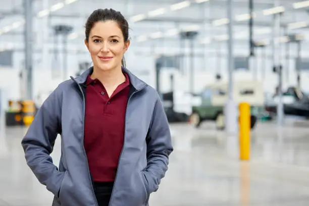 Portrait of confident supervisor with hands in jacket's pockets. Female engineer is standing in industry. Smiling professional is in automobile showroom.