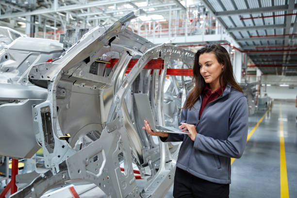 Maintenance engineer using laptop by car chassis Female maintenance engineer using laptop by car chassis. Technologist is using internet by vehicle body in industry. Professional is manufacturing automobile in factory. car engineer stock pictures, royalty-free photos & images