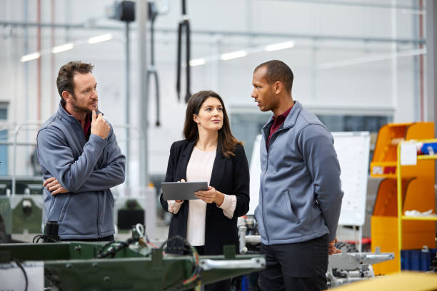 Professionals discussing in car factory Automobile engineer discussing with colleagues in car factory. Multi-ethnic male and female professionals are standing at car production line. They are in automotive industry. showroom photos stock pictures, royalty-free photos & images