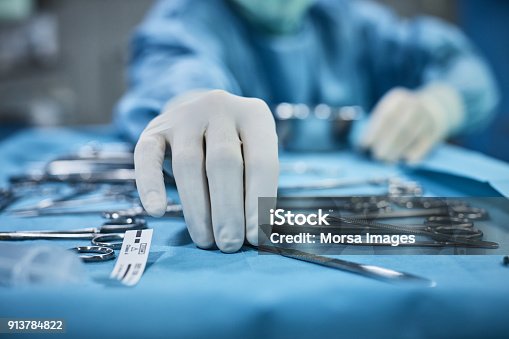 istock Surgeon picking up surgical tool from tray 913784822