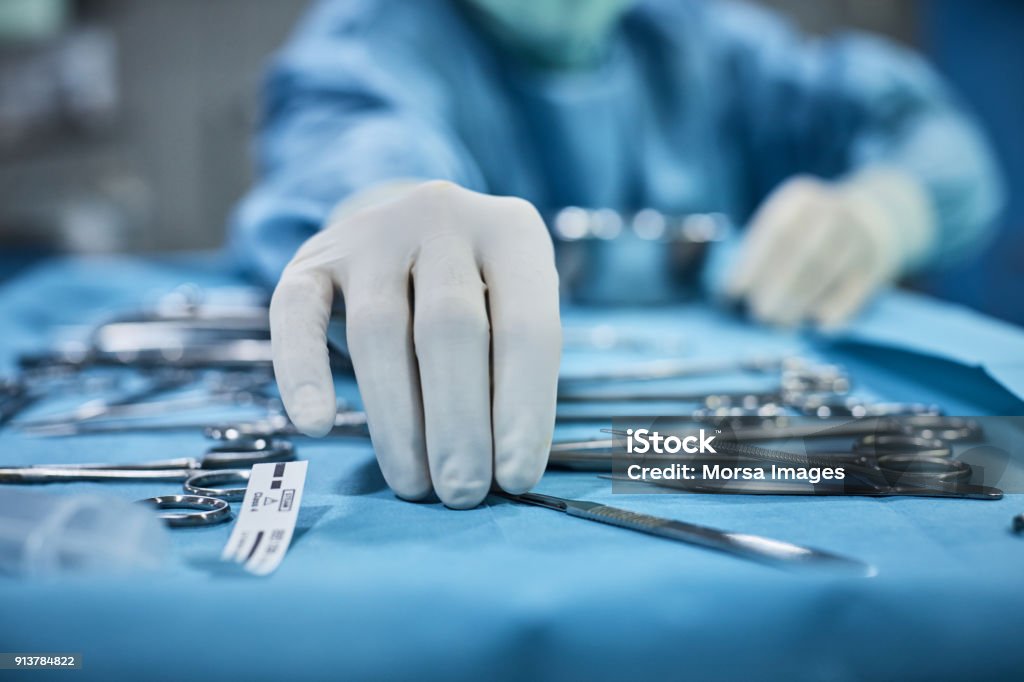 Surgeon picking up surgical tool from tray Surgeon picking up surgical tool from tray. Surgeon is preparing for surgery in operating room. He is in a hospital. Surgery Stock Photo