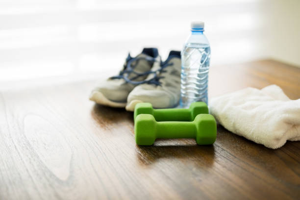 Fitness equipment on wooden table Fitness and active lifestyles concept. Dumbbells, sport shoes, bottle of water and towel on wooden table bottled water on table stock pictures, royalty-free photos & images