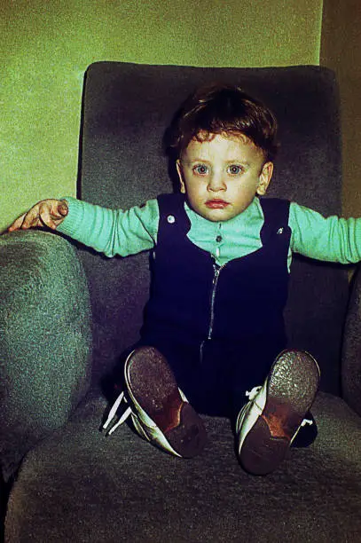 vintage  image of a cute kid looking at camera with big eyes and sitting on a big armchair
