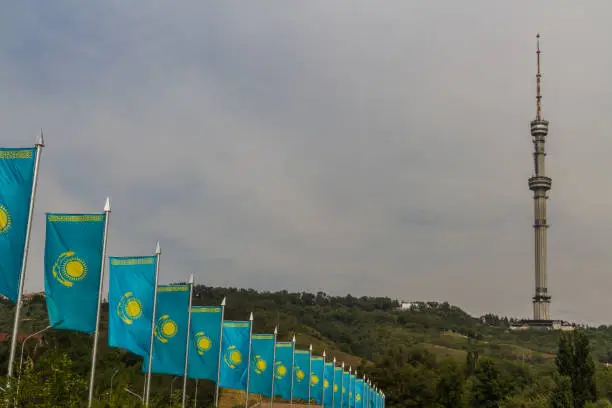 Line of blue and yellow Kazakh flags in wind, with Kok-Tobe television tower in the background Almaty, Kazakhstan, Asia.
