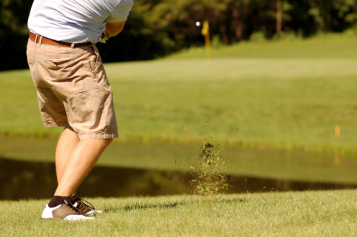 Golfer is driving the ball towards the hole which is over the pond. 