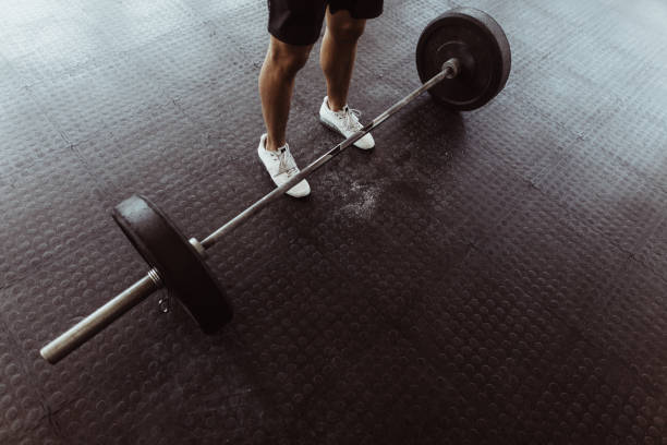 Male athlete exercising with heavy weights at gym.  High angle view of man feet with barbell on gym floor.