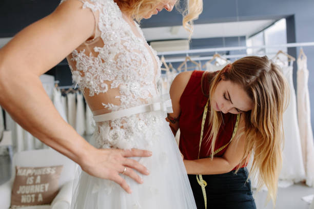 Skillful designer fitting bridal gown to bride Skillful dress designer fitting wedding gown to woman in her boutique. Woman making adjustments to bridal gown in fashion designer studio. bridal shop photos stock pictures, royalty-free photos & images