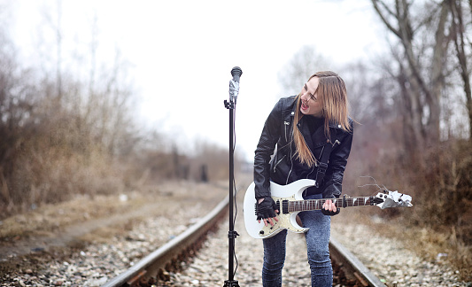 Beautiful young girl rocker with electric guitar. A rock musician girl in a leather jacket with a guitar sings. A rock band soloist plays the guitar and screams into microphone.
