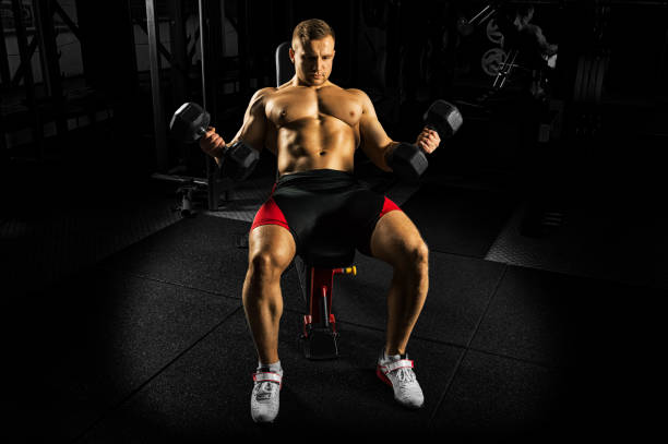 Professional athlete makes an exercise on the biceps by lifting dumbbells while sitting on the bench. stock photo