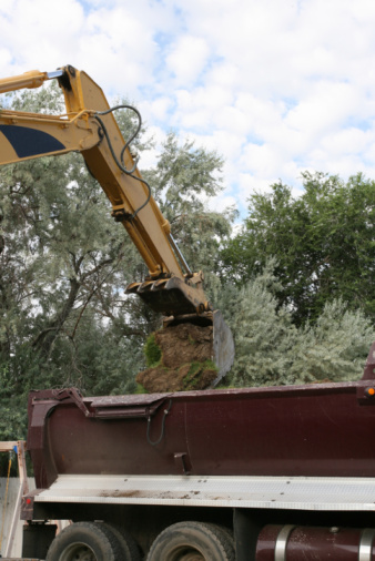 Arm and bucket of a trackhoe moving dirt into a dump truck.