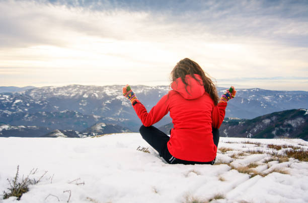 Girl meditating on snow covered mountain top at sunset