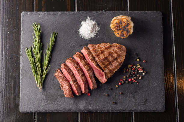 istock Sliced prime ribeye steak on black stone plate. Medium degree of steak doneness. With rosemary and peppers. Fork and knife. 913846292