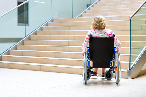 woman on wheelchair standing before stairs looking up for help