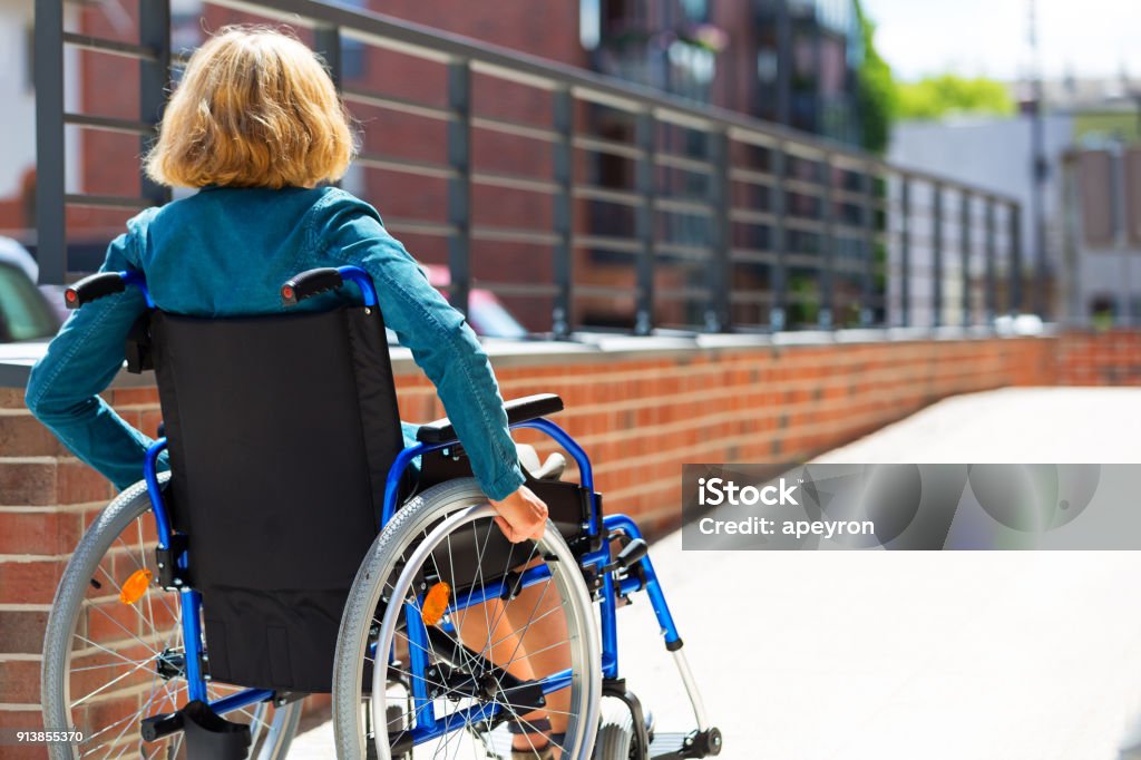 woman on wheelchair entering the platform adult woman on wheelchair entering the platform or driveway - view from back Disability Stock Photo