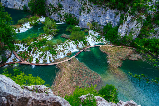 Plitvice Lakes and watrefalls aerial view. Massive waterfalls down to green lake. Cliff in background. Water is surrounded with lush foliage.