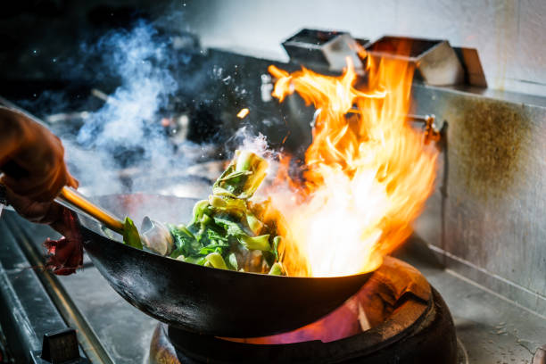 koch in der küche am herd mit hohen brennenden flammen - gourmet küche stock-fotos und bilder