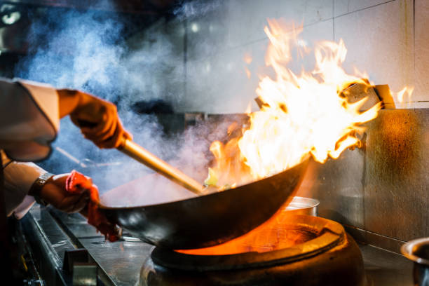 Chef in restaurant kitchen at stove with high burning flames
