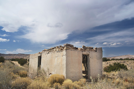 Deserted old stone building in the red sand desert landscape of New Mexico with a cloudless blue sky.