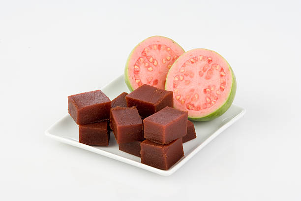 Small cubes of guava jam in front of two halves of a guava guava fruit and paste on a white plate guava photos stock pictures, royalty-free photos & images
