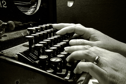 Hands typing on old typewriter keyboard B&W image