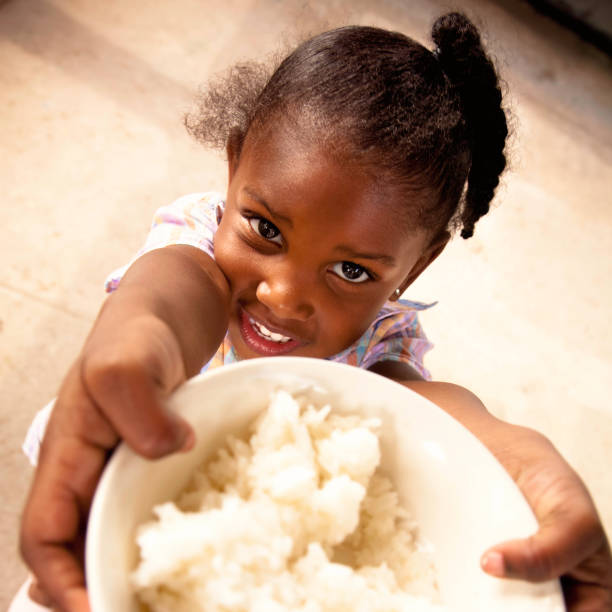Little girl holds bowl of rice Adorable preschool age African American girl smiles while holding a bowl filled with white rice. rice food staple stock pictures, royalty-free photos & images