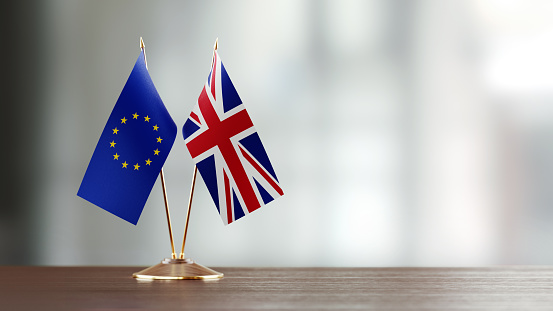 European Union and British flag pair on desk over defocused background. Horizontal composition with copy space and selective focus.