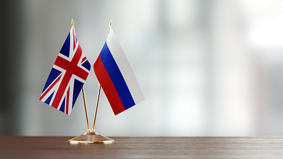 Russian and British flag pair on desk over defocused background. Horizontal composition with copy space and selective focus.
