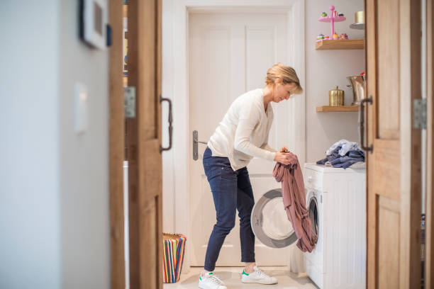 donna matura che carica i vestiti in lavatrice - wash stand foto e immagini stock