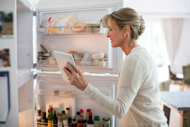 istock Woman with tablet PC looking into refrigerator 913980450