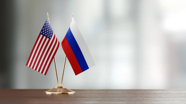 American and Russian flag pair on desk over defocused background. Horizontal composition with copy space and selective focus.