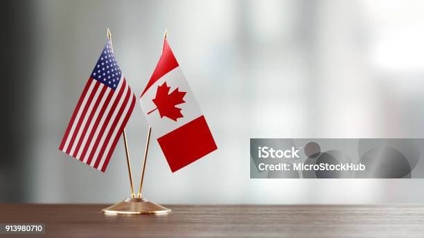 American And Canadian Flag Pair On A Desk Over Defocused Background Stock Photo - Download Image Now