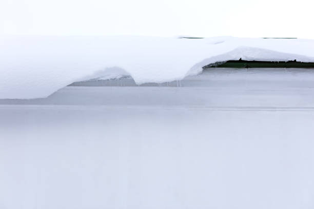 melting snow overhanging on the roof down to white building wall