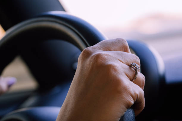 Image of female hands on a steering wheel, steadily driving down a road.
