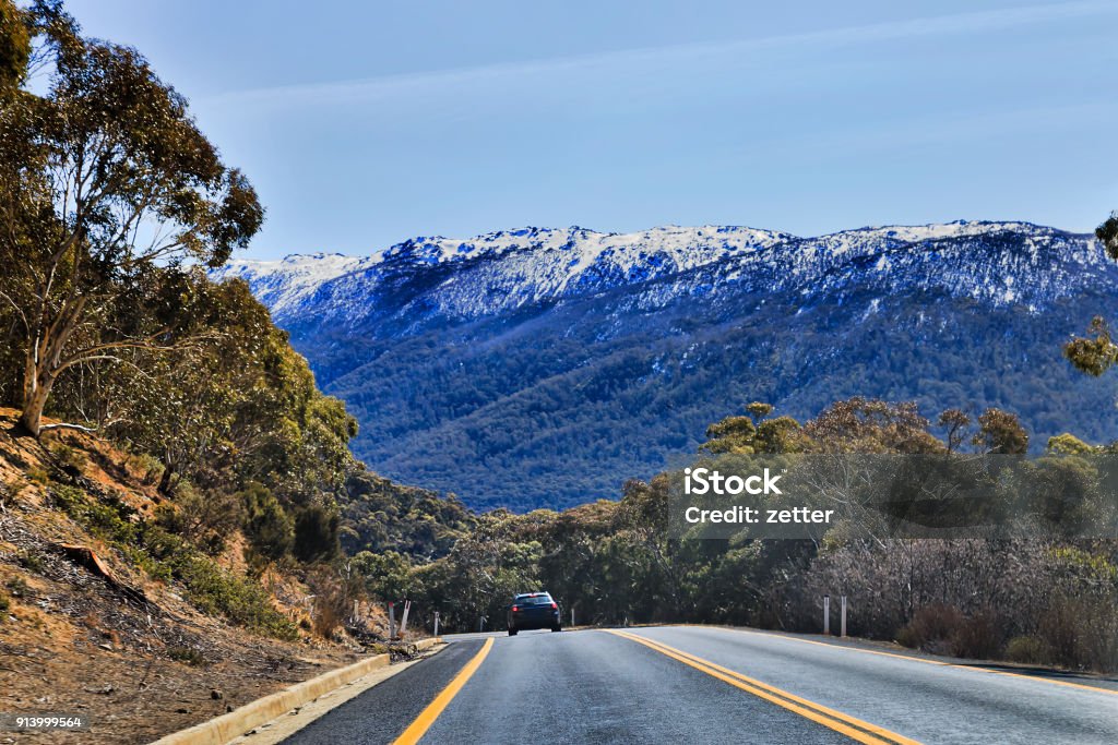 Thredbo Blue Sky WInding thredbo road in Snowy mountains national park leading to THredbo town popular ski resort in NSW, Australia. Beautiful sunny winter day with snow covered rocks of mountains ranges and snow-gum trees. Kosciuszko National Park Stock Photo