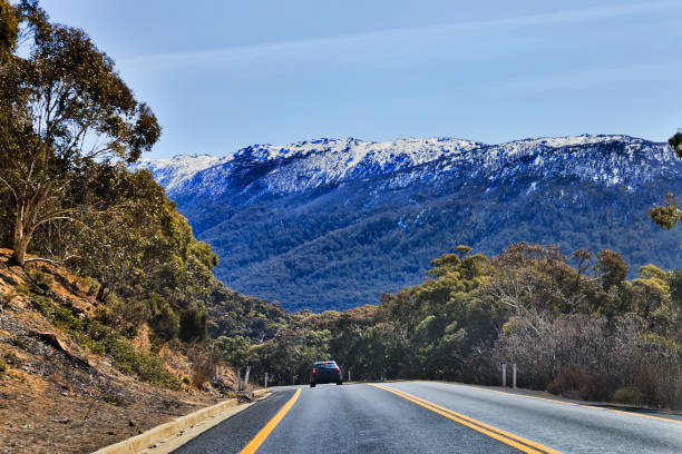 Thredbo Blue Sky WInding thredbo road in Snowy mountains national park leading to THredbo town popular ski resort in NSW, Australia. Beautiful sunny winter day with snow covered rocks of mountains ranges and snow-gum trees. all weather running track stock pictures, royalty-free photos & images