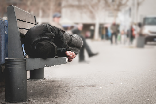Pobre hombre sin hogar o refugiados durmiendo en el Banco de madera en la calle urbano de la ciudad, concepto de documental social, enfoque selectivo photo