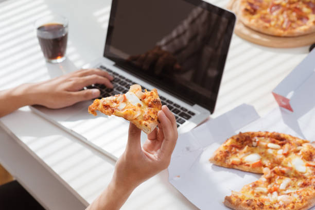 istock Cropped image of an asian man having lunch with pizza while working at his desk. 914011074