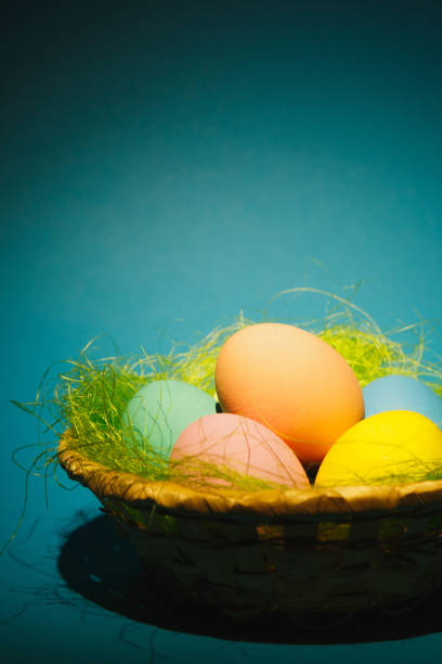 istock Colorful pastel monophonic traditional painted Easter eggs in basket with green grass on dark blue background with black shadows, silhouette, light. Copy space for advertisement. With place for text 914015328